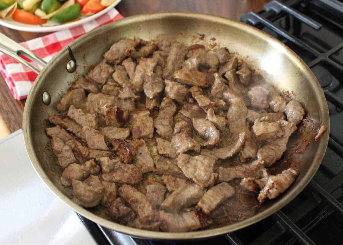 thinly sliced beef cooking in a large pan on the stove