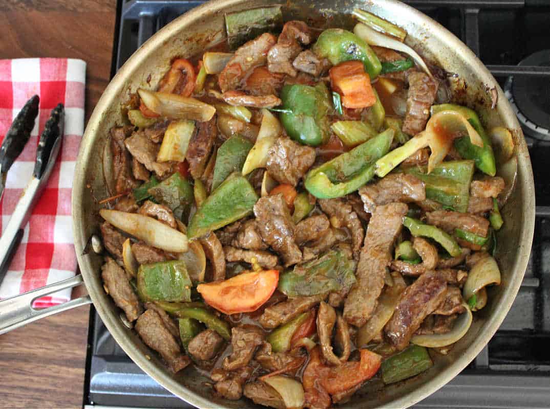 saucy beef tomato stir fry in a large pan on the stove top
