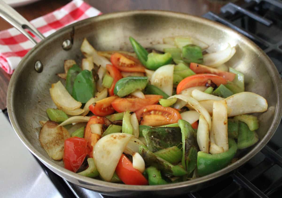 tomatoes, onions, bell pepper, and celery being stir fried in a large pan