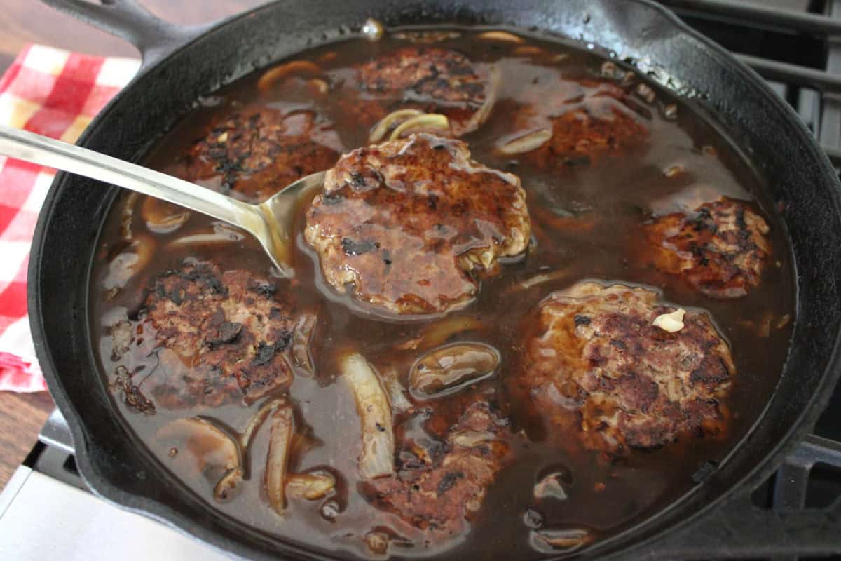 beef patties simmering in a rich brown gravy on the stove