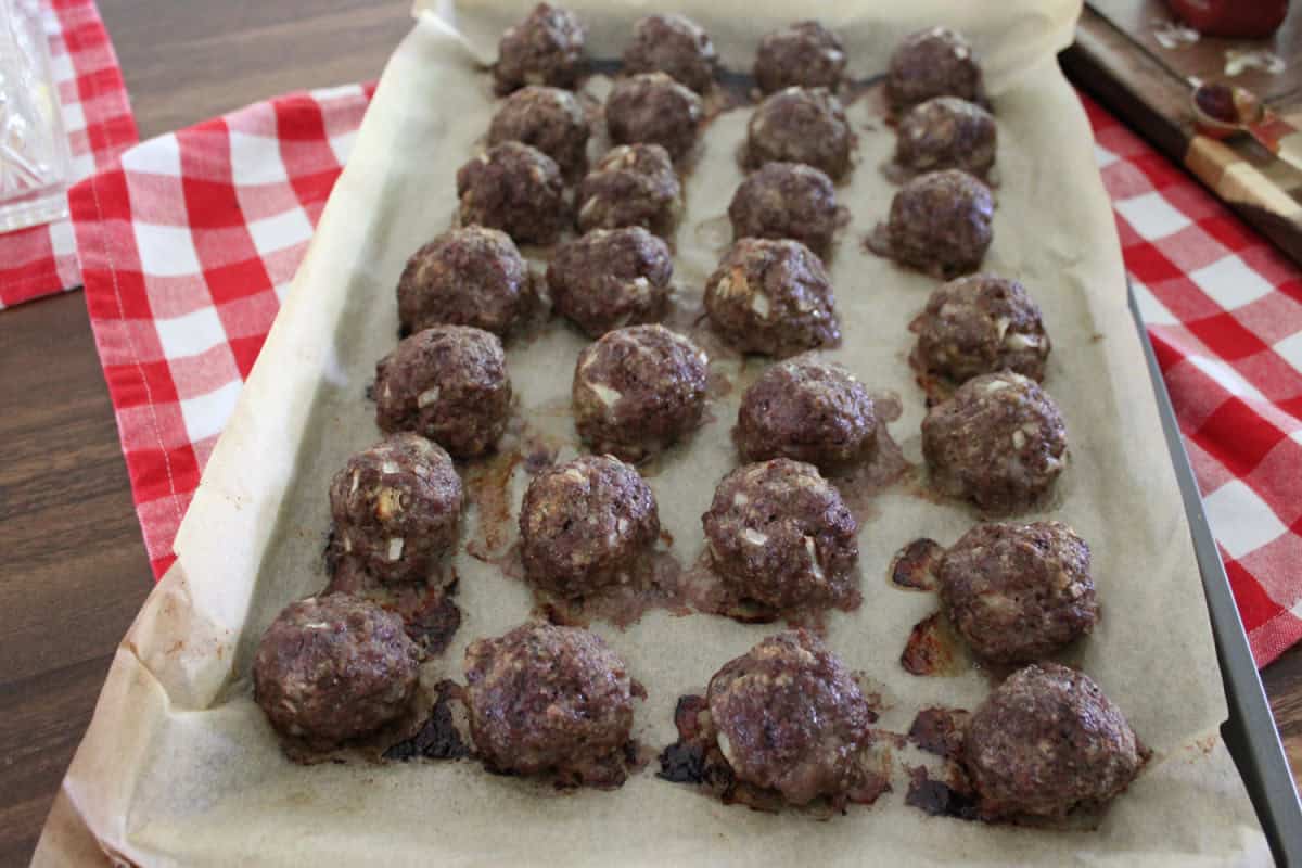 cooked meatballs on parchment paper lined cookie sheet