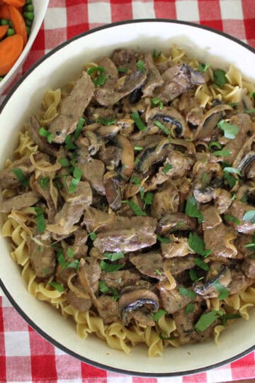 beef stroganoff on top off egg noodles with a side of peas and carrots