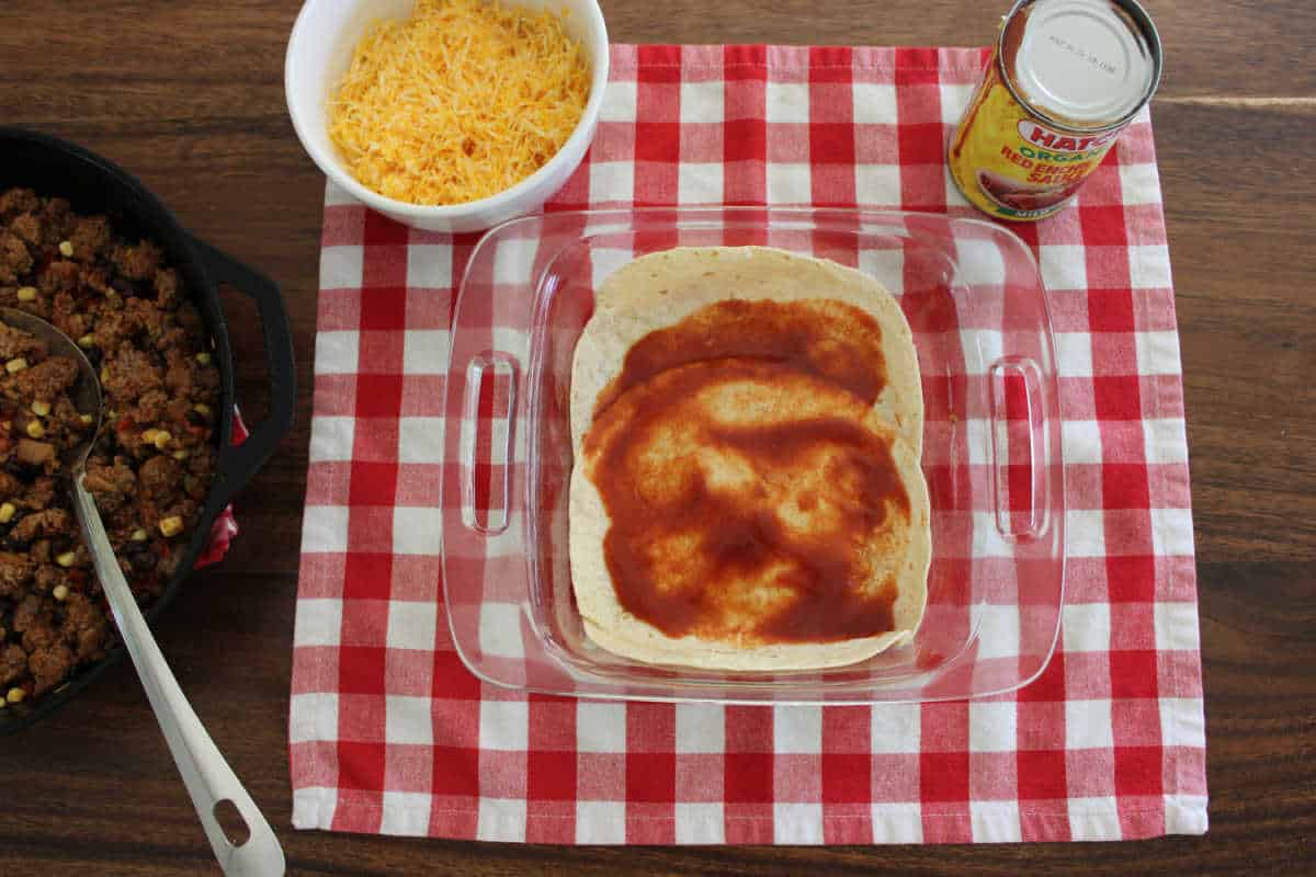 red enchilada sauce being spread over tortillas