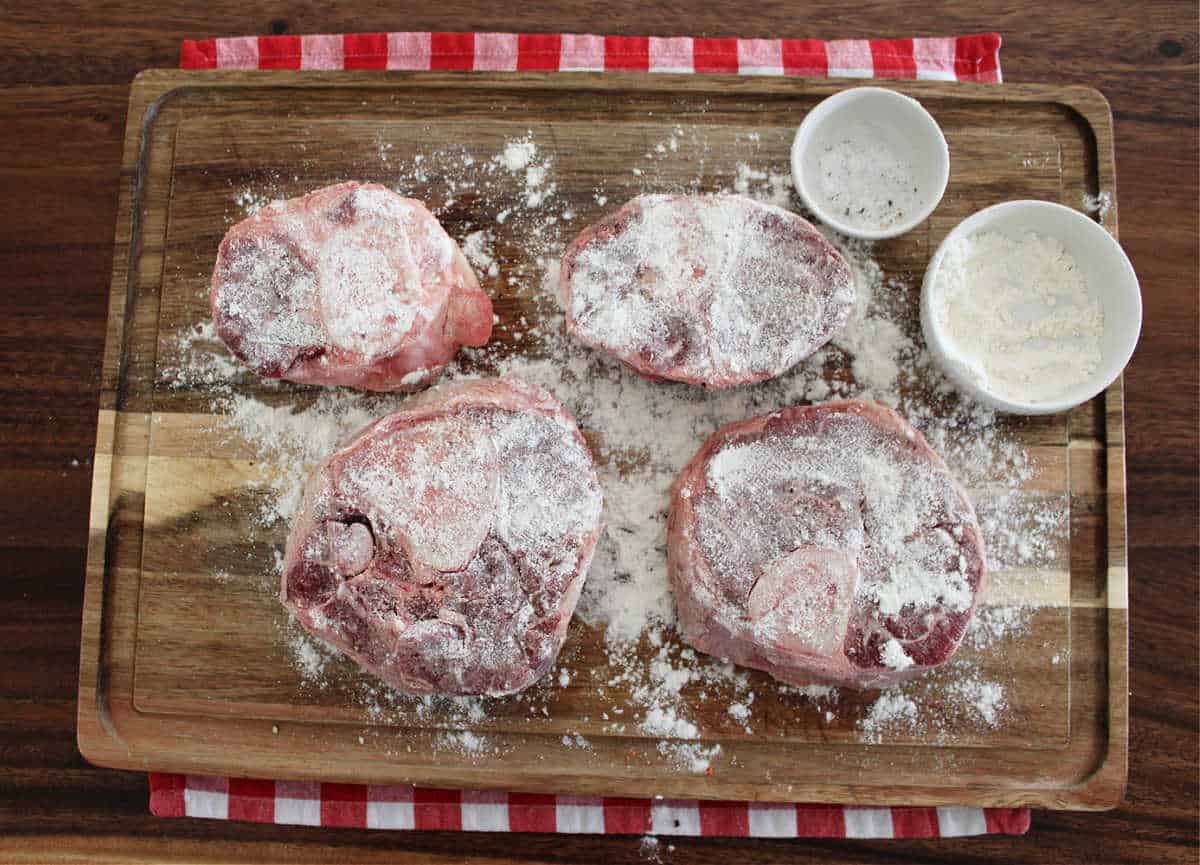 four beef shanks dusted with flour on a wood cutting board 