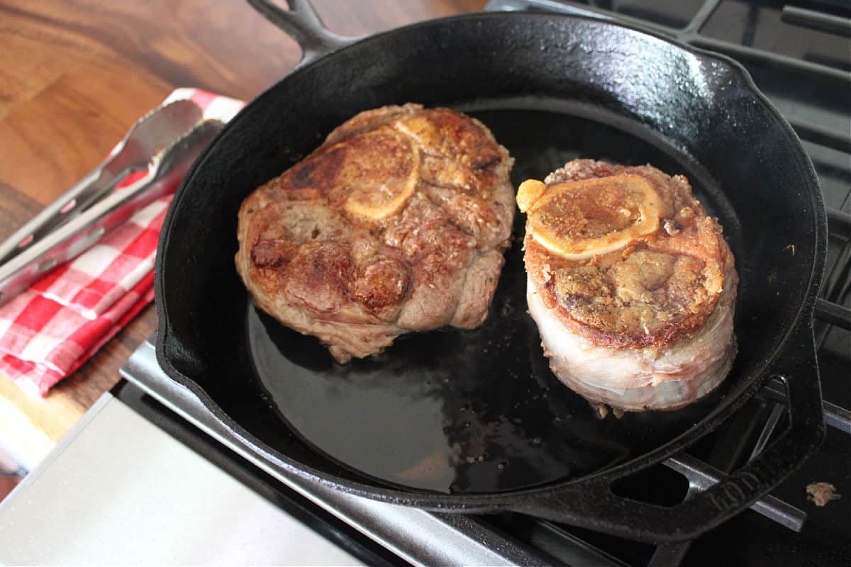 two beef shanks being browned in a cast iron skillet