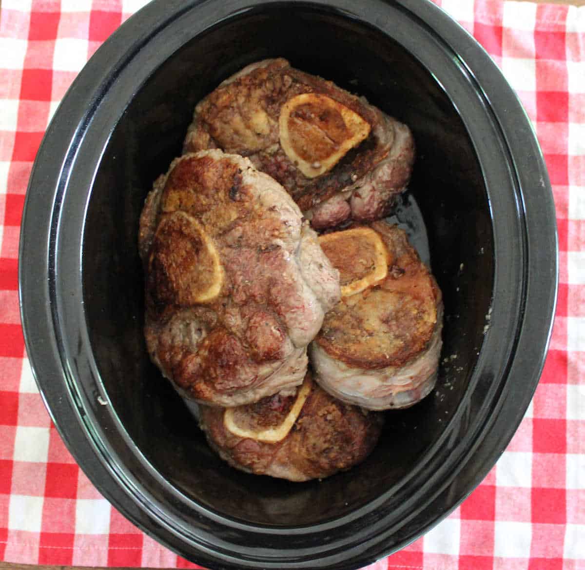 four browned beef shanks in a black crock pot