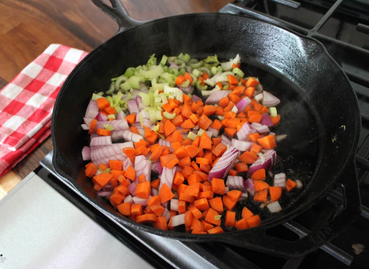 celery carrots and red onion being sauteed in a cast iron skillet