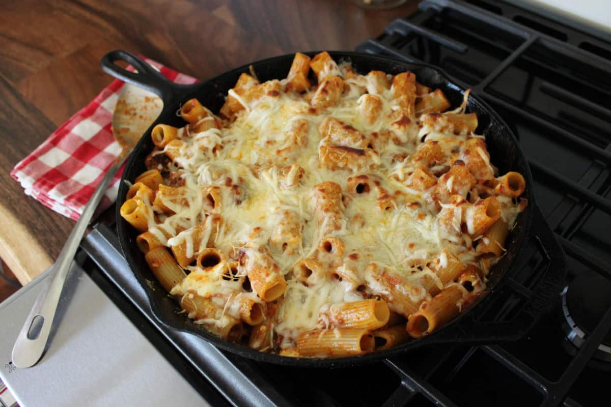 browned and cheesy rigatoni pasta bake in a black cast iron skillet