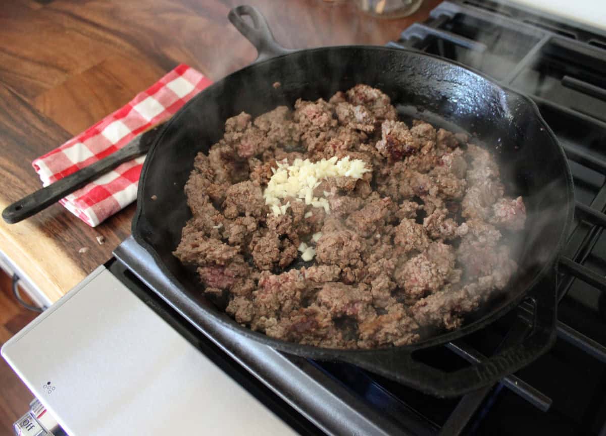 browned ground beef in a cast iron skillet with minced garlic