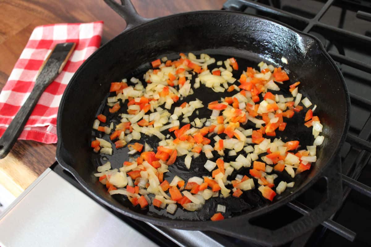 onions and red bell peppers cooking in a cast iron skillet