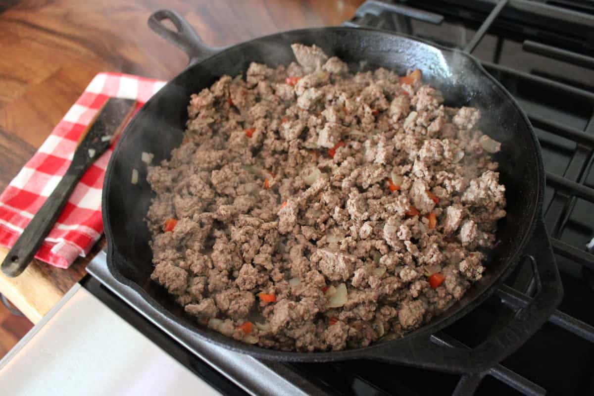 browned ground beef with onions and red bell peppers in a cast iron skillet