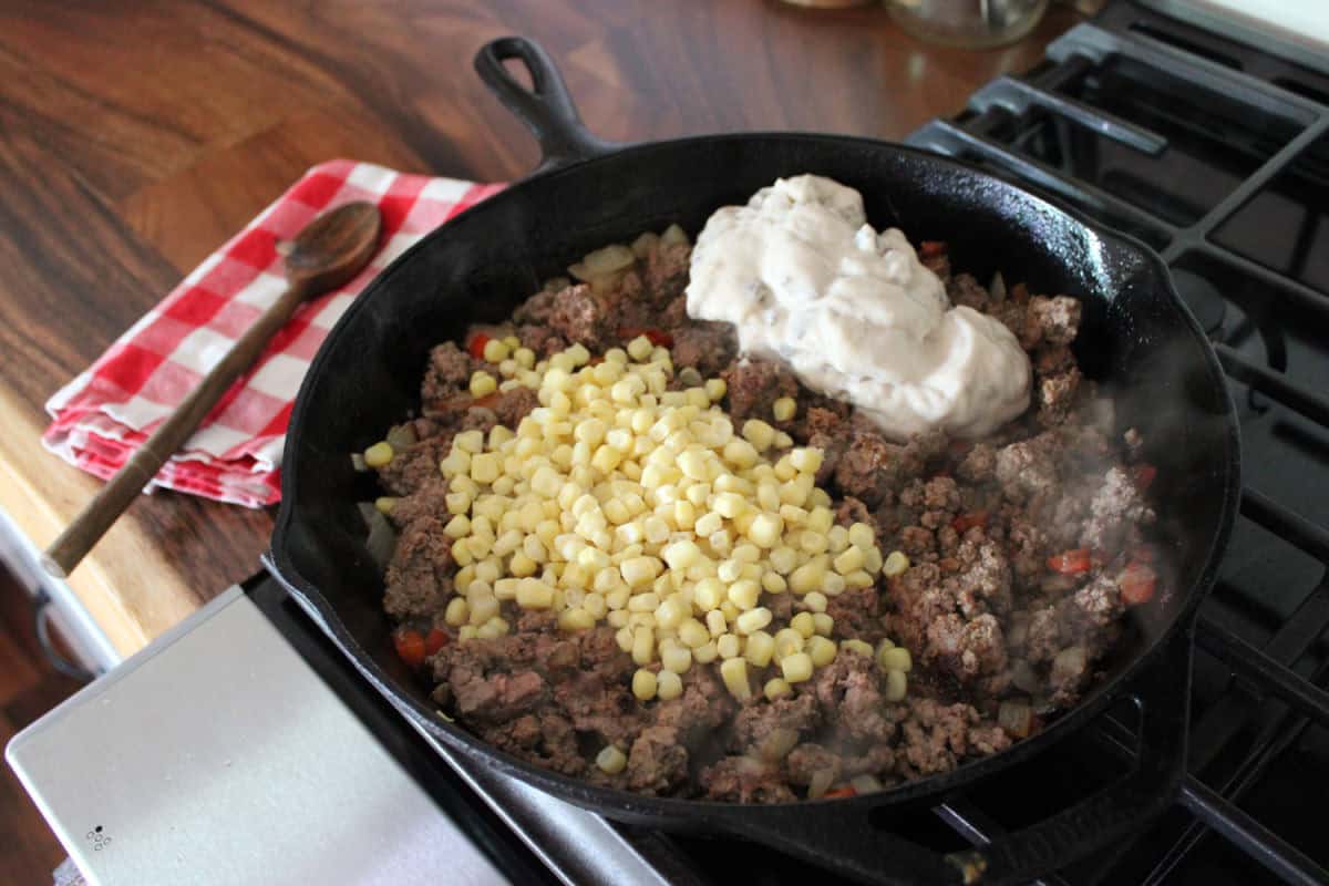 frozen corn and can of mushroom soup on seasoned ground beef 