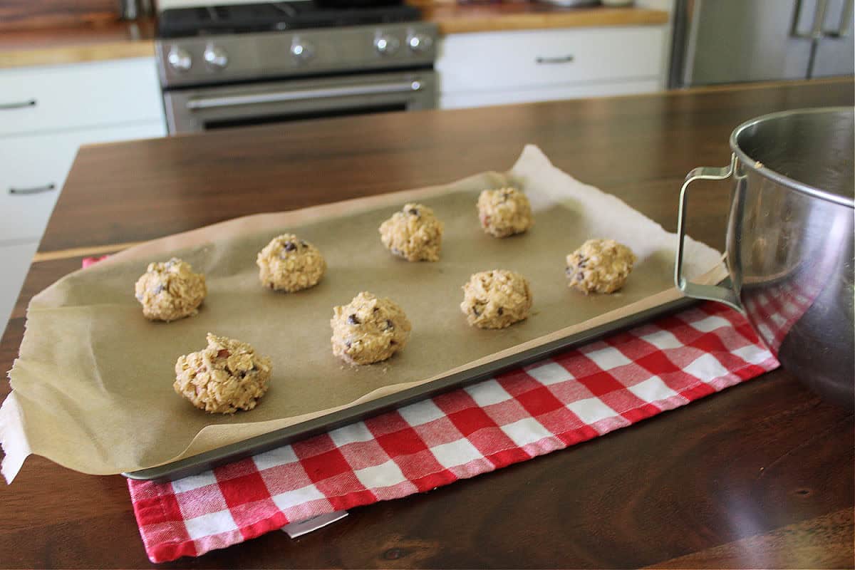raw cowboy cookie dough scooped into large balls on a lined cookie sheet
