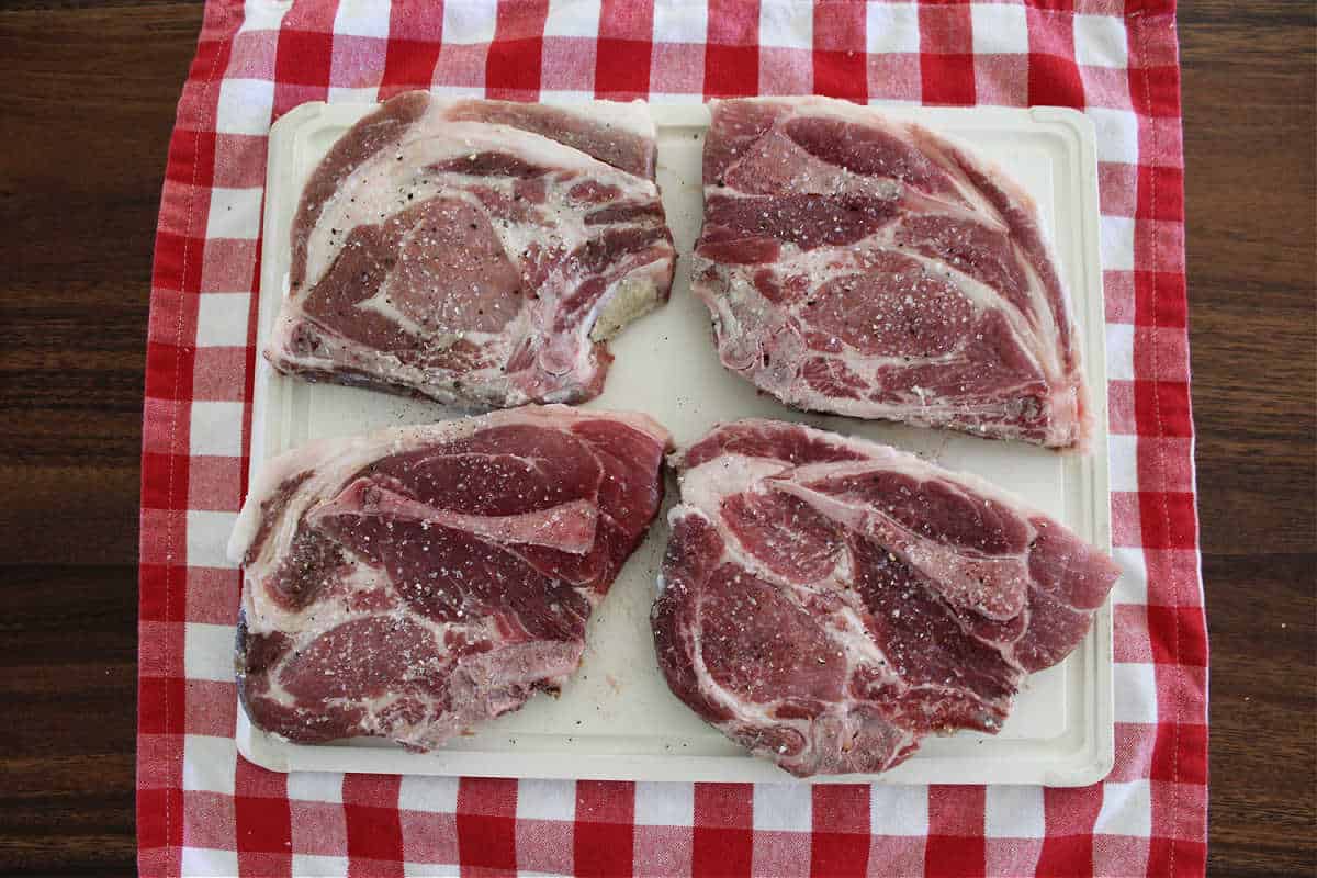 Four seasoned pork chops on a white cutting board.