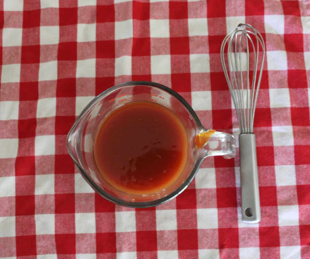 A glass measuring cup with a red sauce in it.