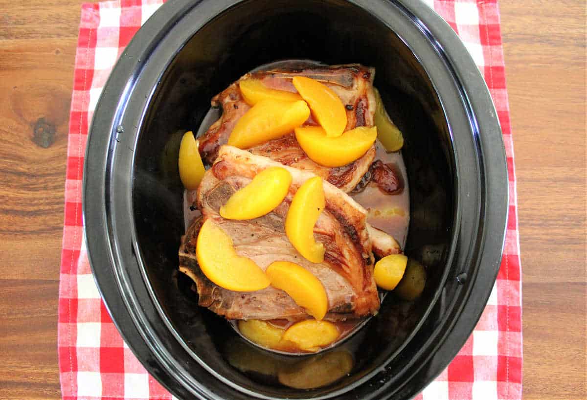 Pork chops and canned peaches in a black slow cooker.
