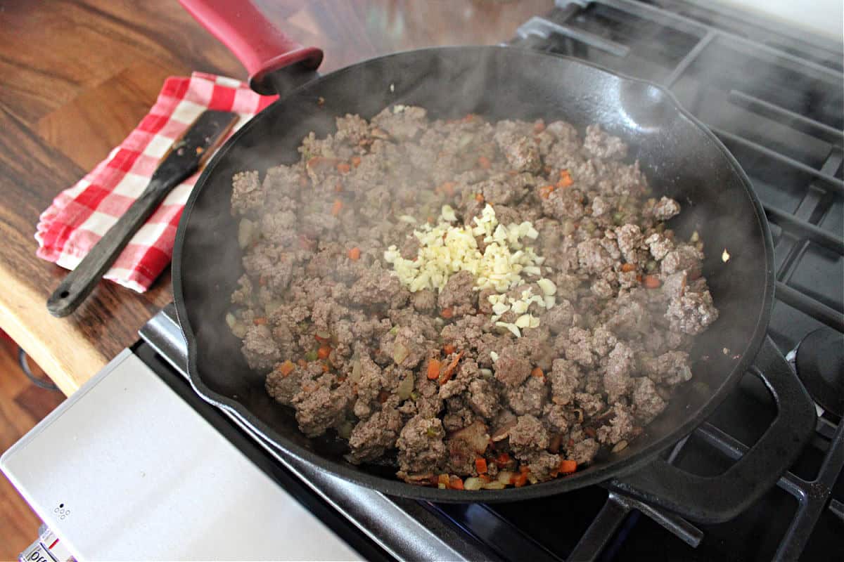 raw minced garlic added to a pan of browned ground venison