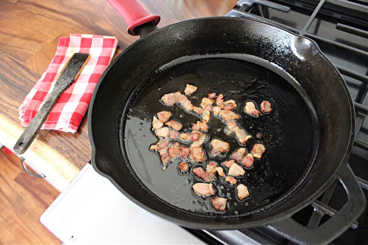 diced bacon being rendered in a black cast iron skillet