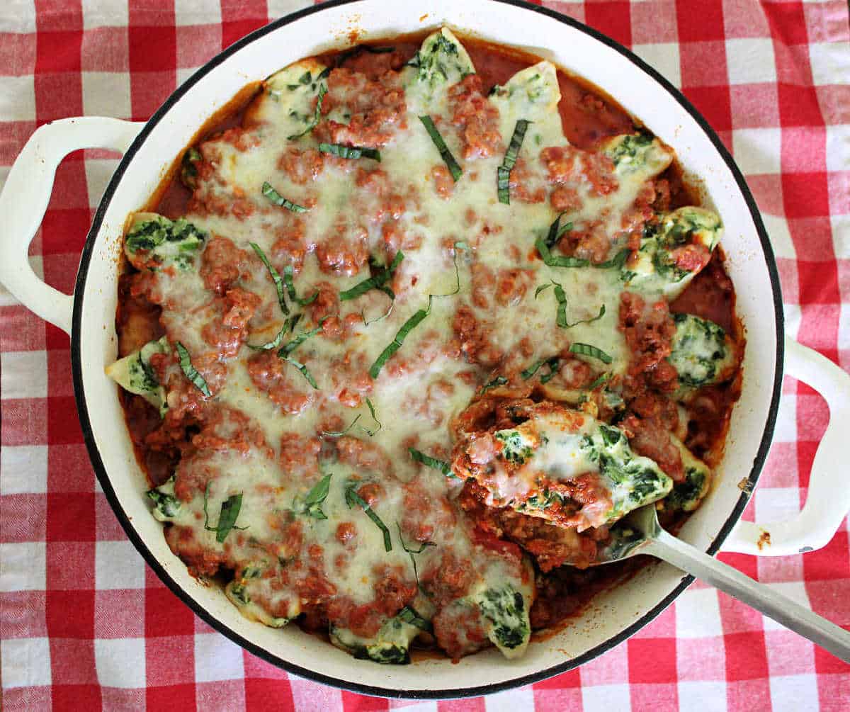 Overhead shot of large white pan with spinach stuffed shells over ground marinara. 