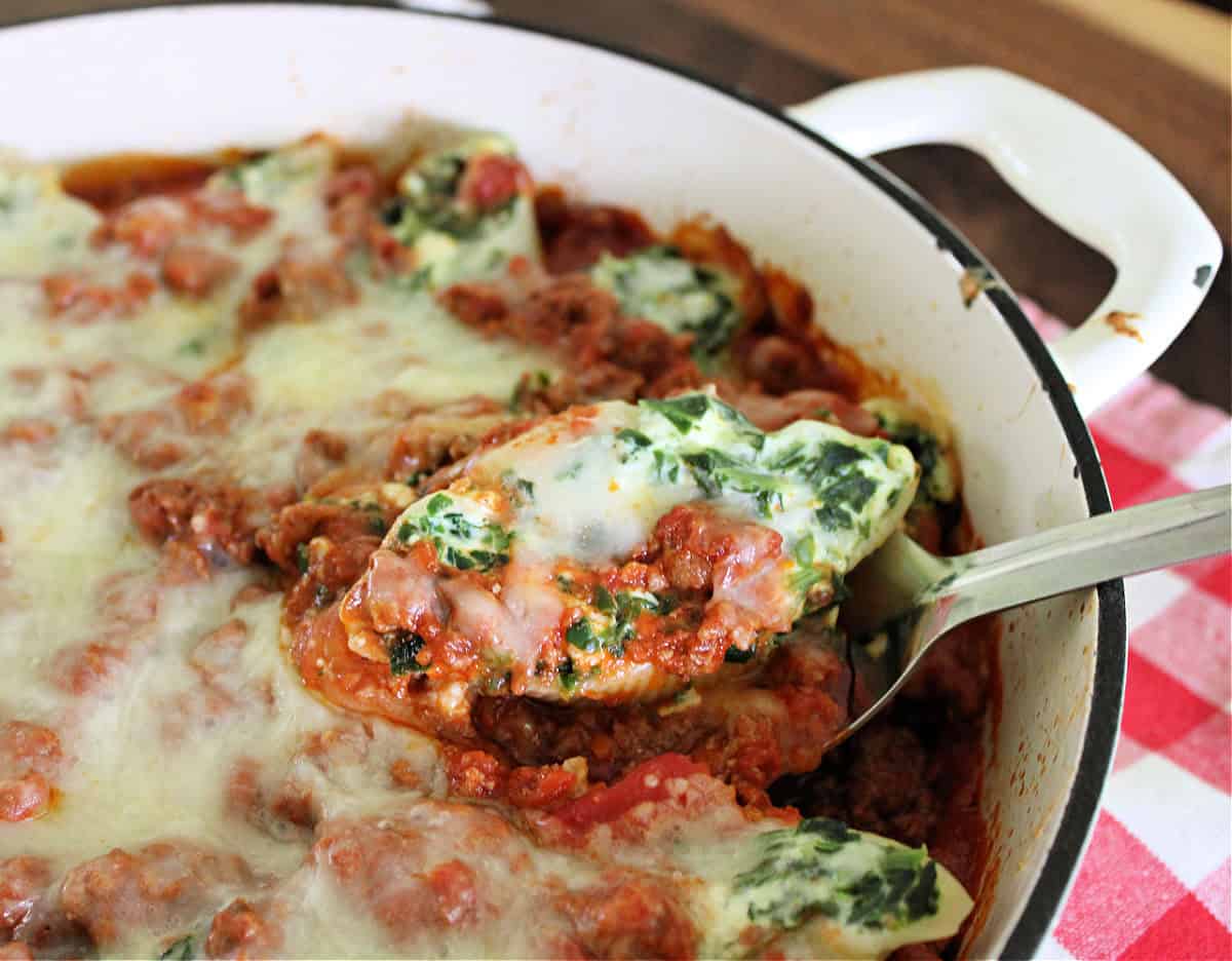 Spinach and ricotta stuffed pasta shells being scooped out of dish.