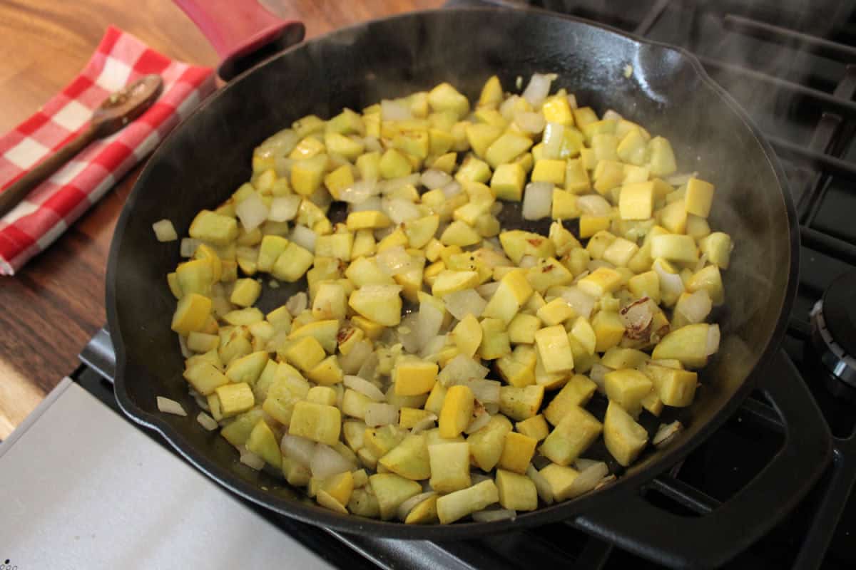 diced yellow squash and onion cooking in black cast iron pan