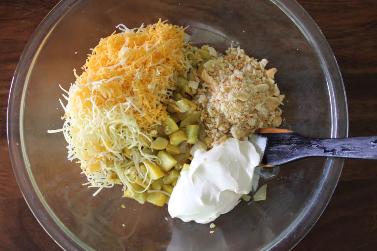 a glass bowl of cooked squash, cheese, ritz crackers, and sour cream