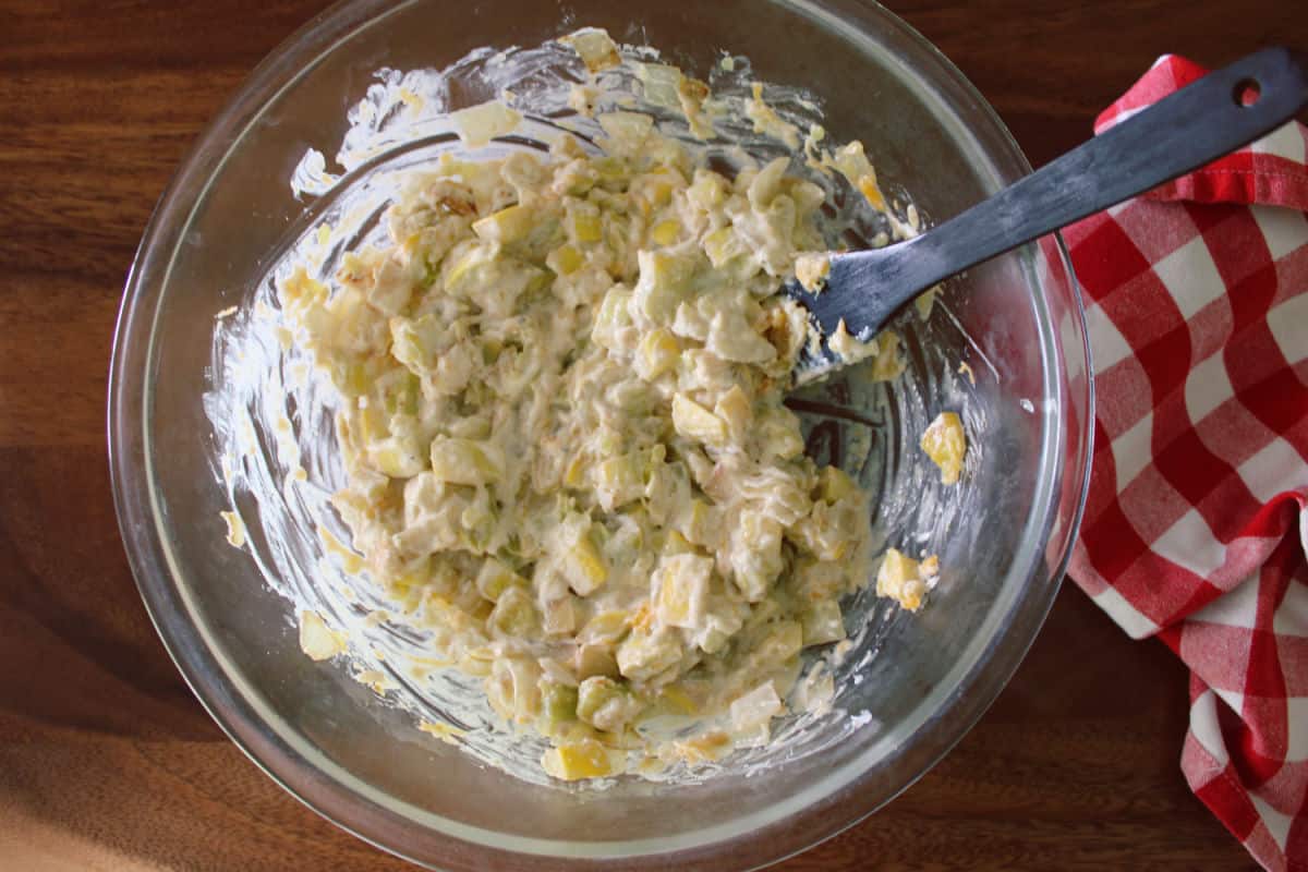 ingredients for yellow squash casserole being mixed together in a glass bowl